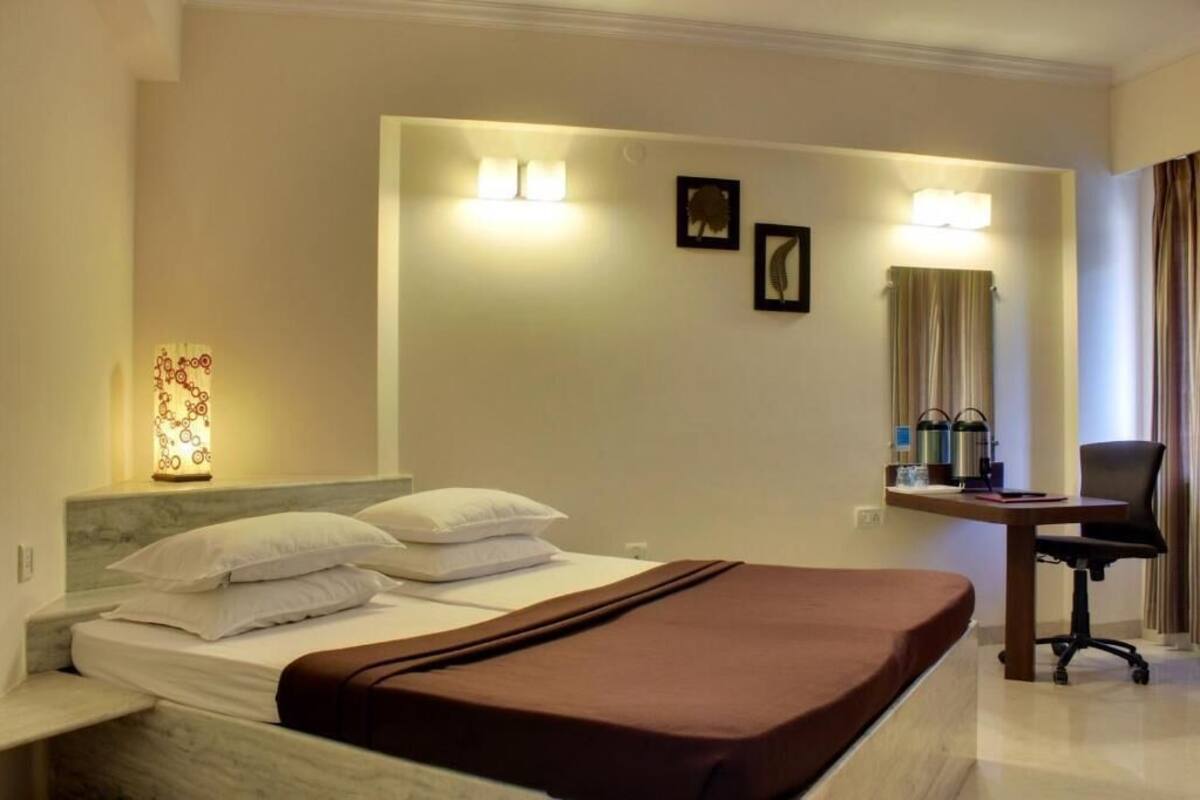 A hotel room with a bed, a desk, a chair, a lamp, and a wall-mounted picture.