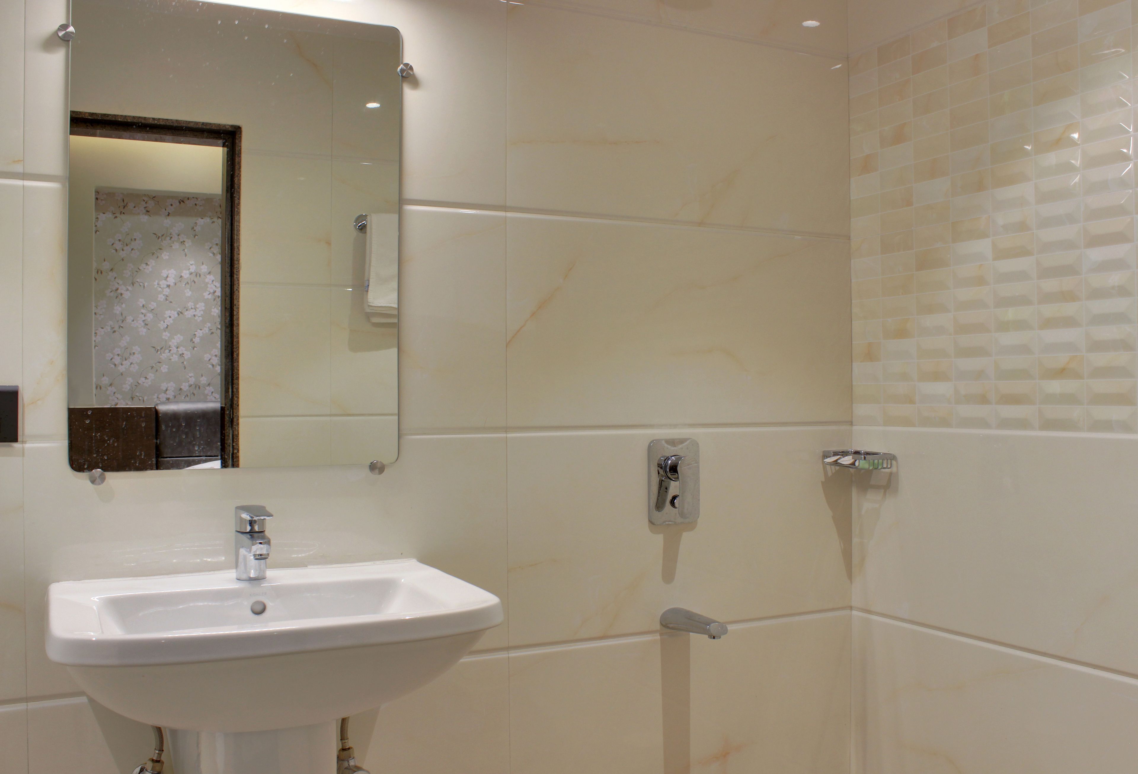 Un baño con un lavamanos blanco, un espejo y paredes con azulejos.