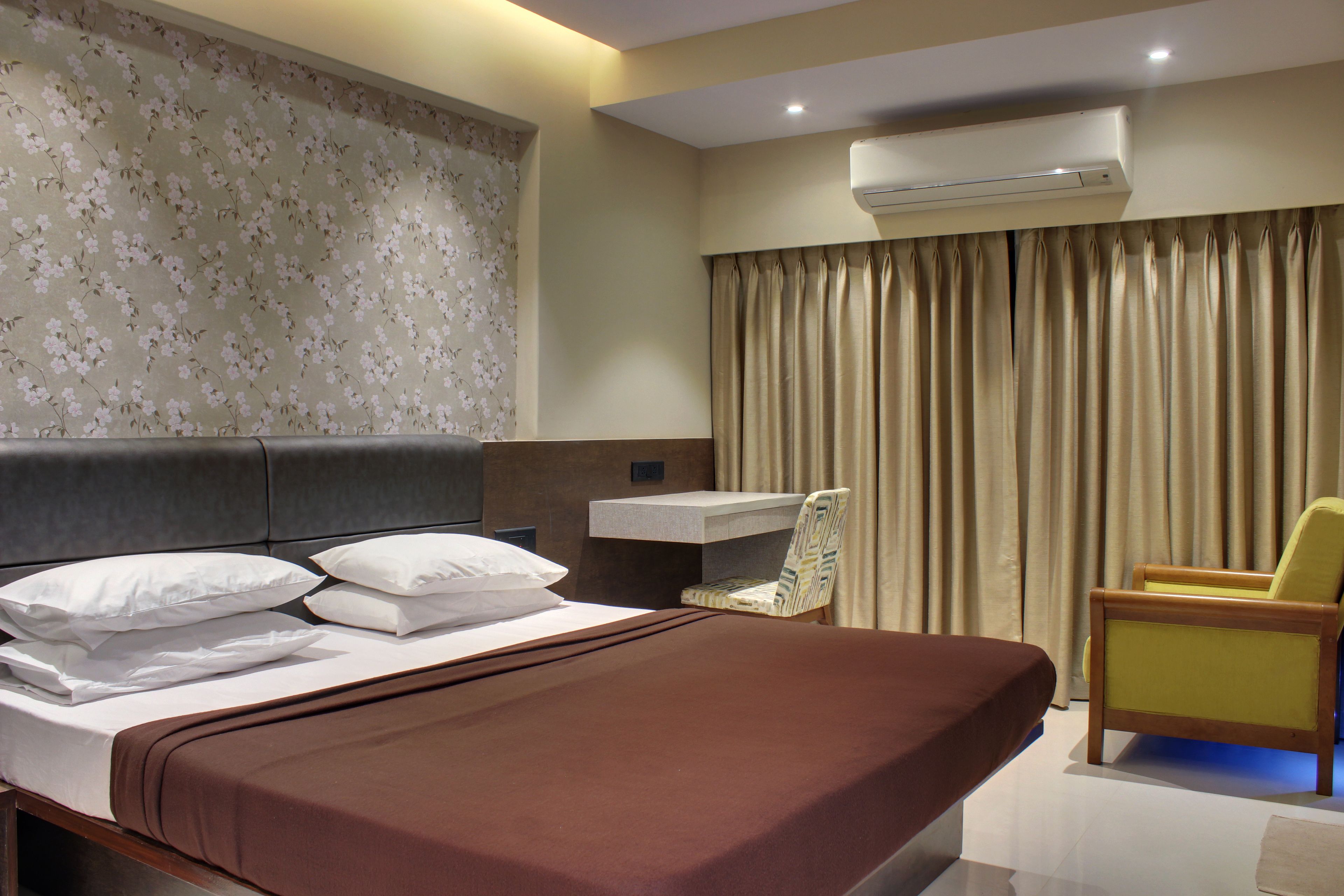 A hotel room with a bed, a desk, a chair, and a window with curtains.