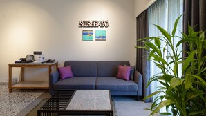 Een woonkamer met een grijze bank, een klein houten tafeltje, een salontafel en een grote groene plant.
