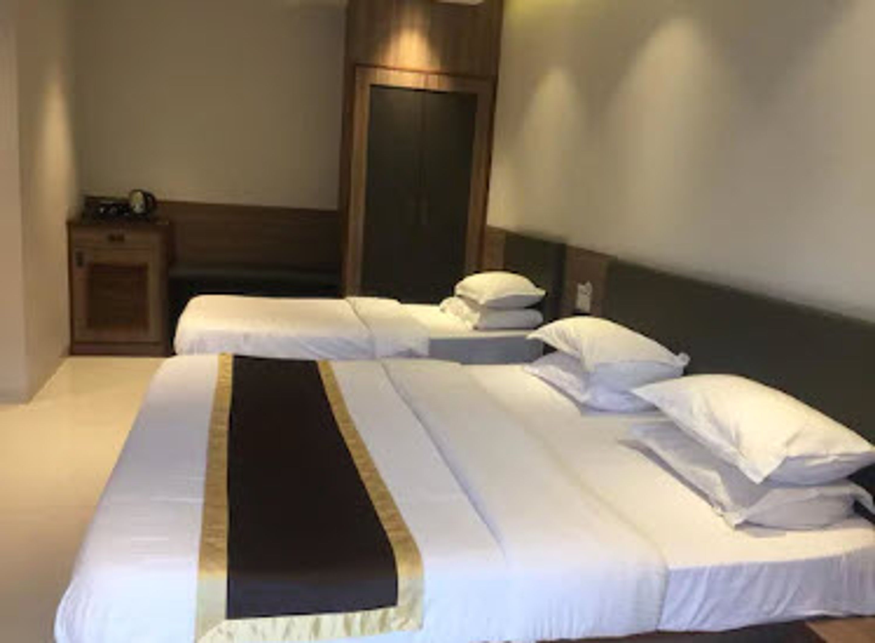 Habitación de hotel con dos camas individuales, un armario de madera y una mesita de noche con lámpara.