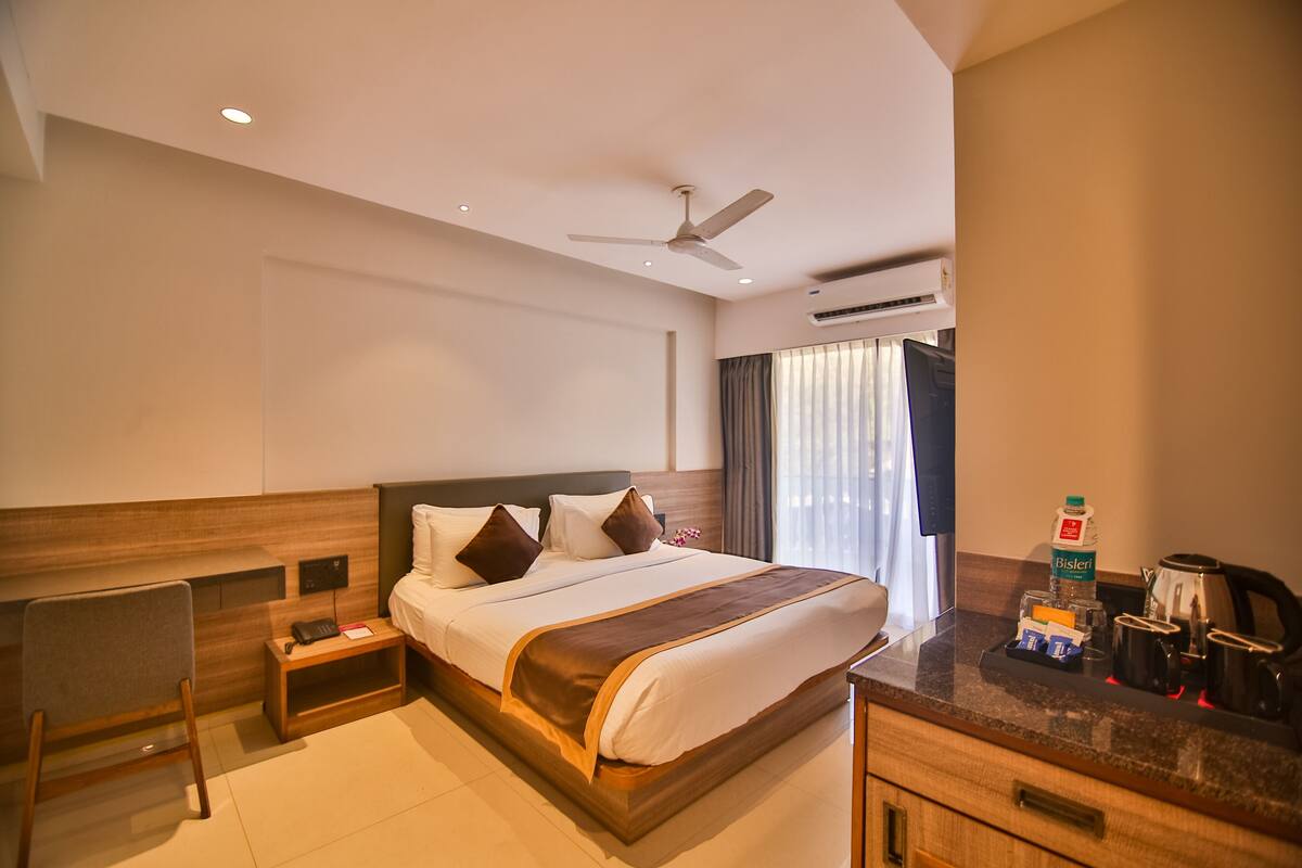 A hotel room with a large bed, a desk, a chair, a nightstand, a ceiling fan, and a coffee maker.