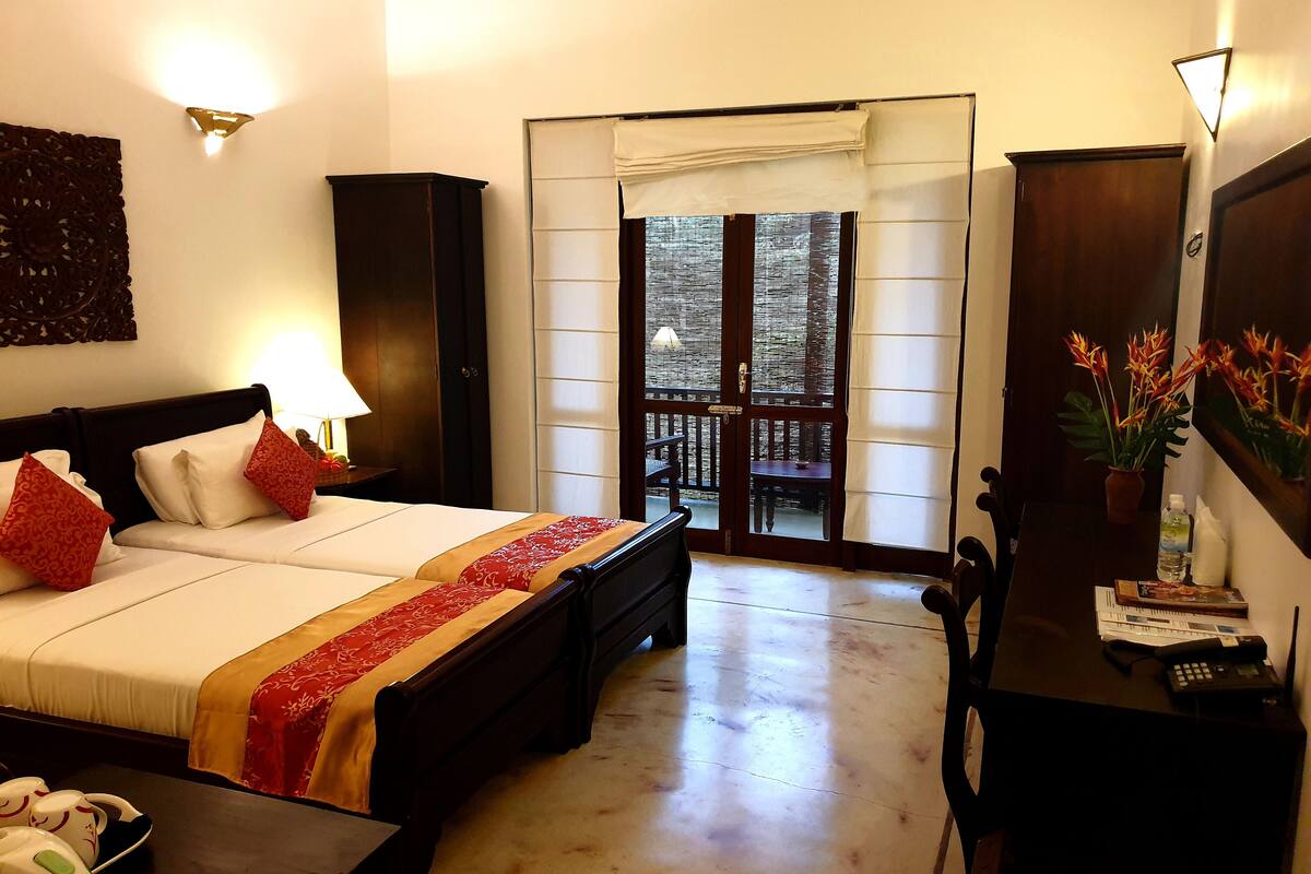 A hotel room with a bed, bedside table, lamp, and a desk with a phone and water bottle.