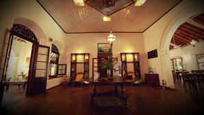 A spacious room with a wooden ceiling, a round table in the center, and a large window on the left. - Nooit Gedacht Heritage Hotel-Original Dutch Governor's House (Unawatuna)