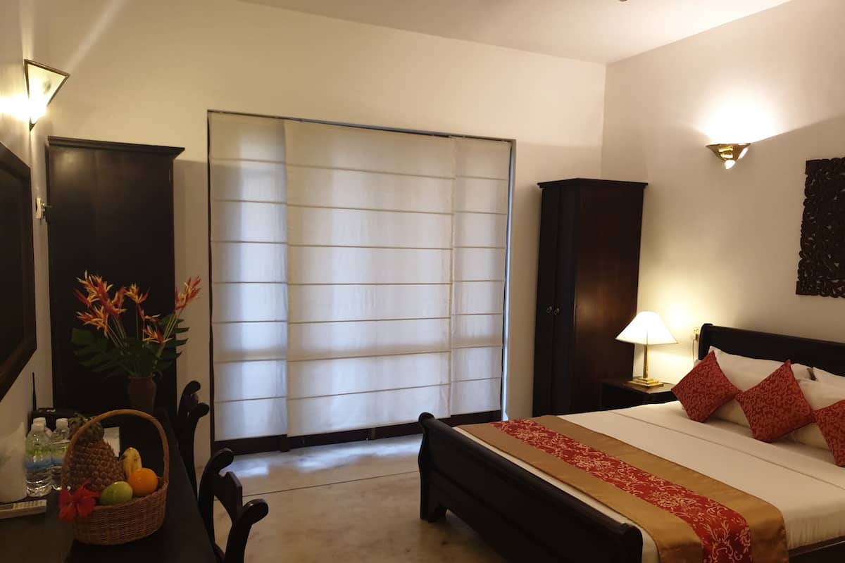A hotel room with a bed, bedside table, lamp, and a window with blinds.