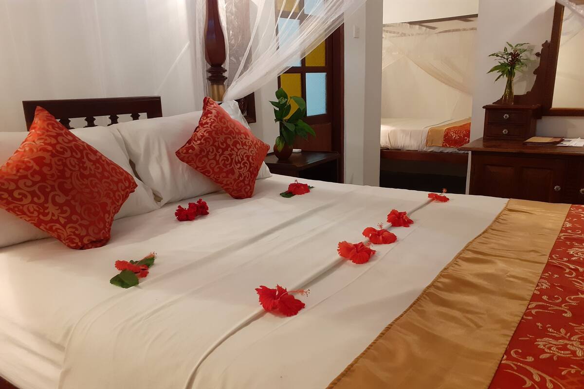 A neatly made bed with white bedding, red patterned pillows, and a decorative red flower garland.