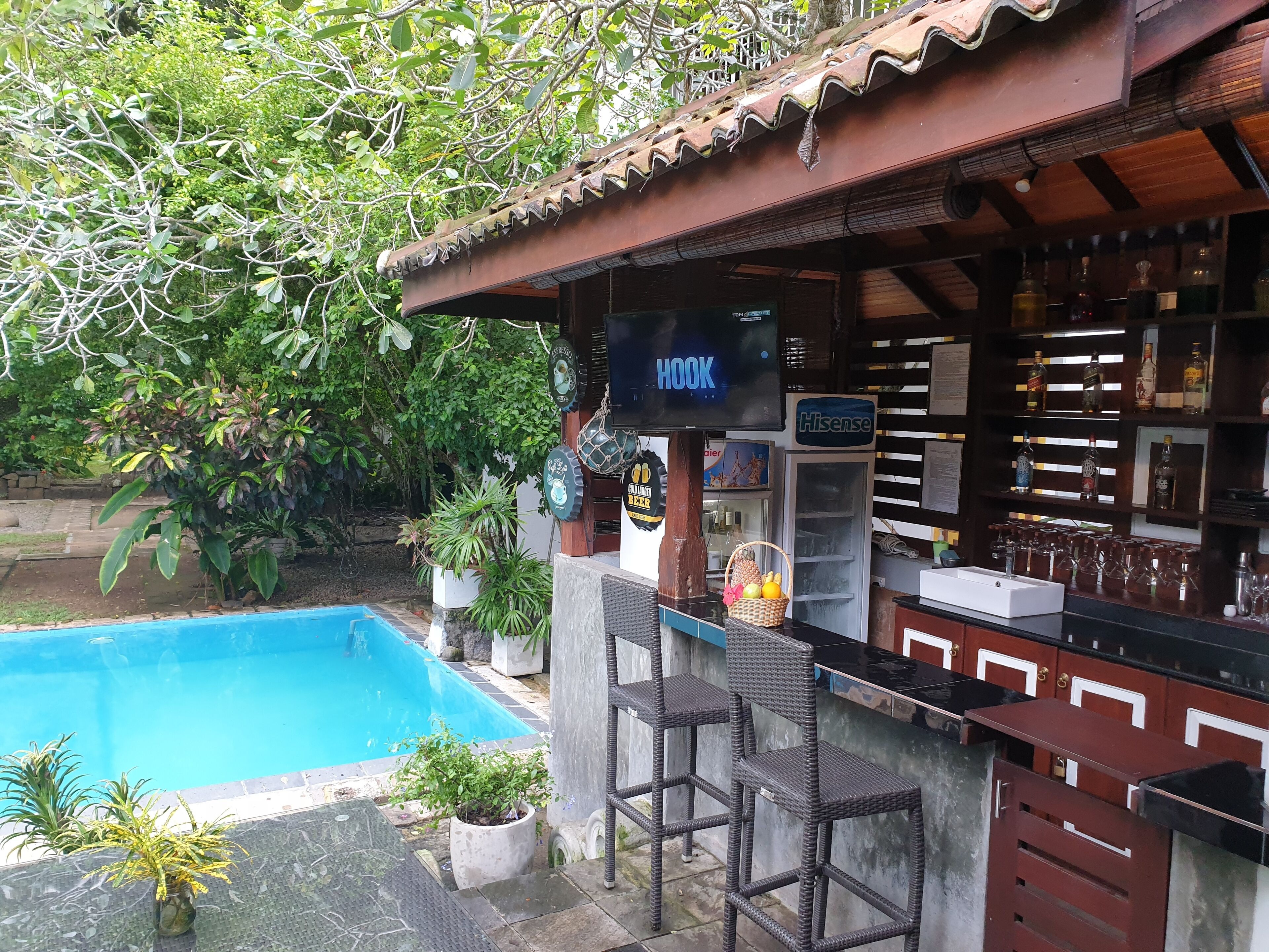 A bar area with a poolside view, featuring a bar counter, seating, and a sign reading "HOOK".