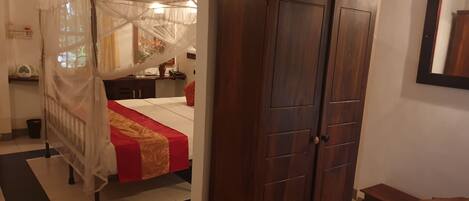 A bedroom with a four-poster bed, a wooden wardrobe, a bench, and a tiled floor.