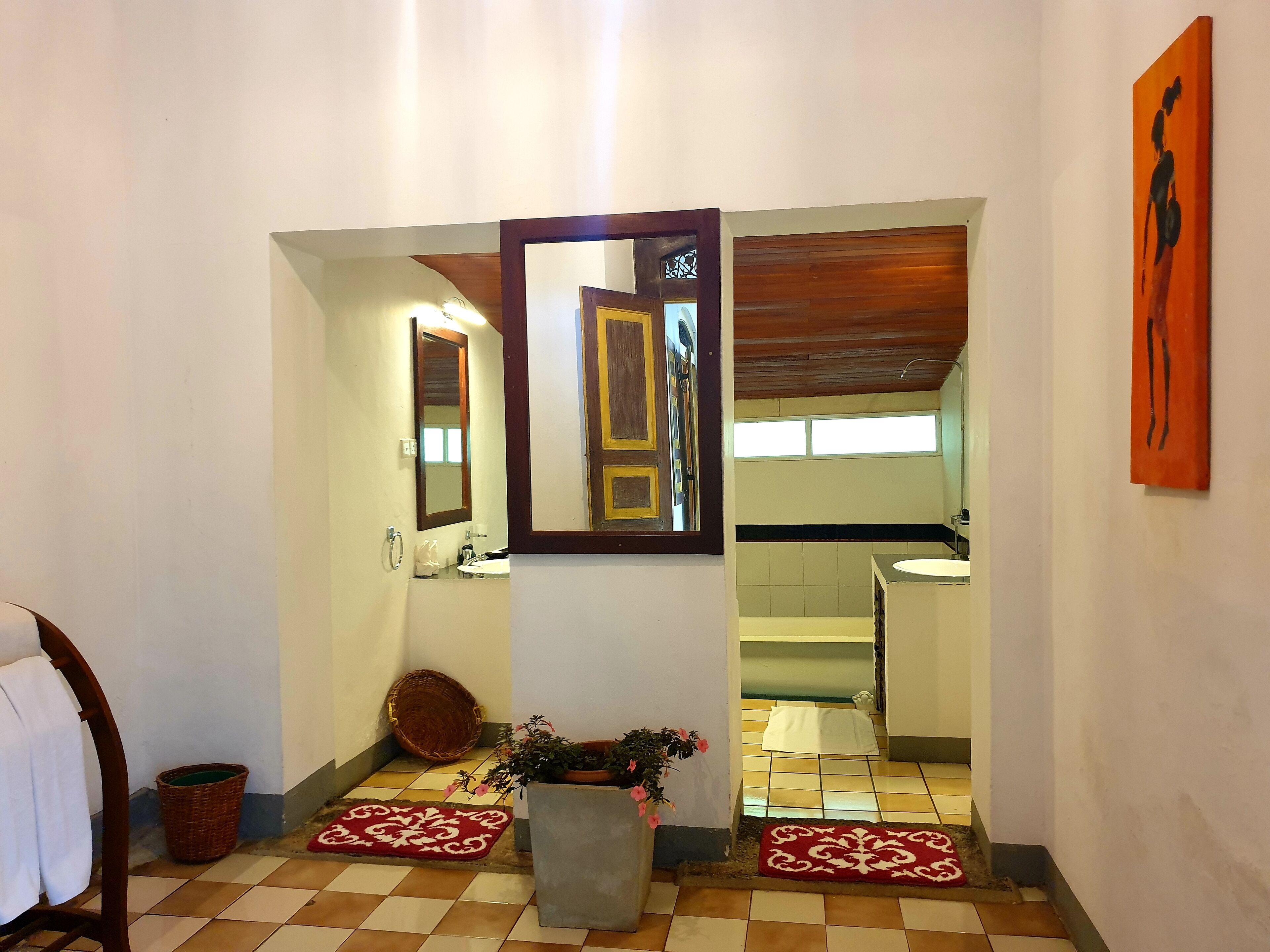 A hallway with a mirror, a potted plant, a red rug, and a wooden door frame.