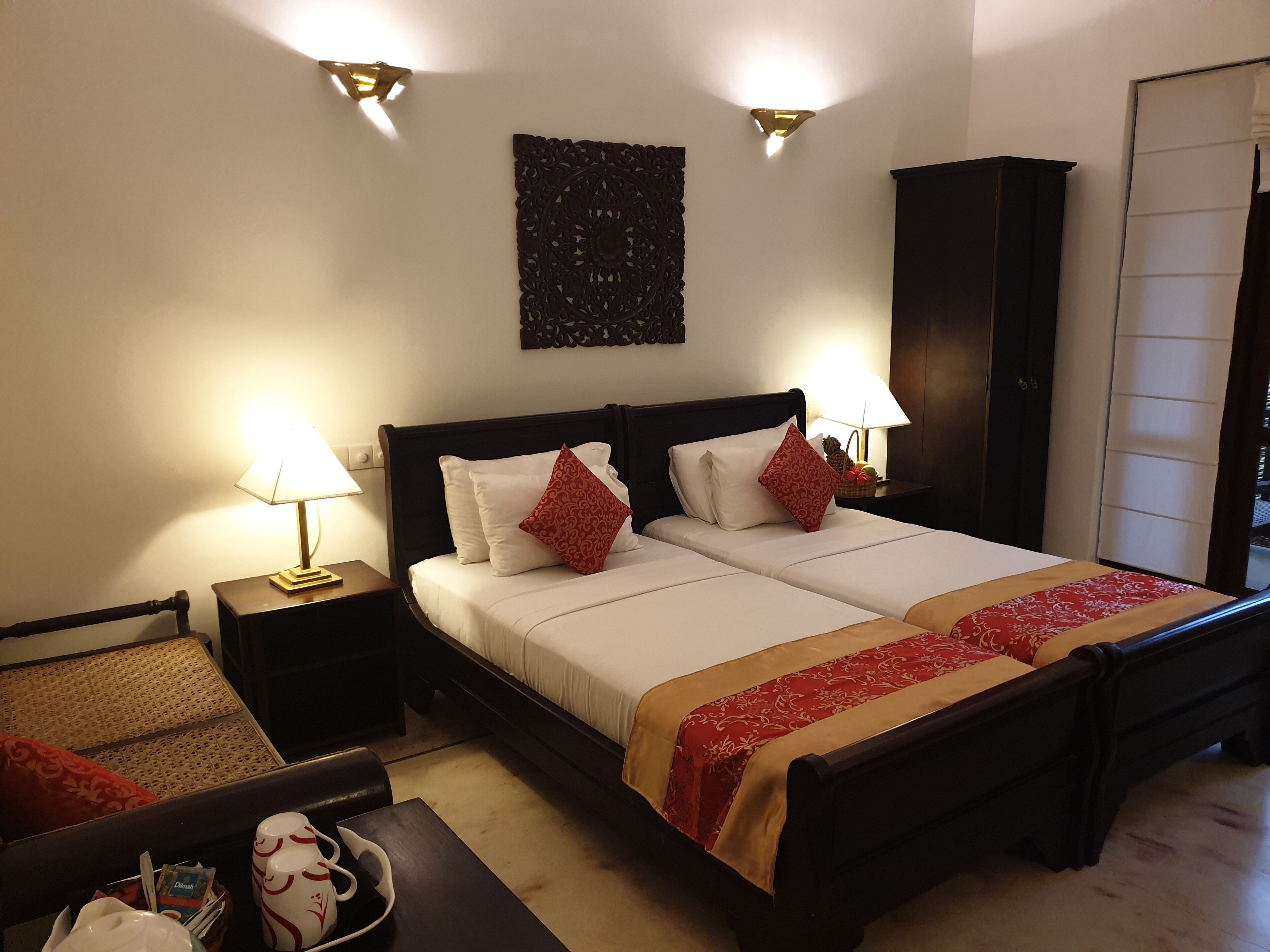 A hotel room with a double bed, two bedside tables with lamps, a decorative wall piece, and a wardrobe.