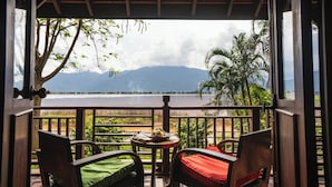 Terraza de madera con dos sillas y una mesita, con vistas a un lago y montañas al fondo.