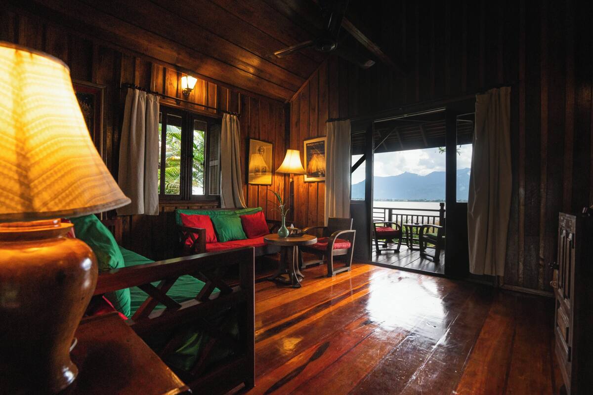 A wooden interior with a sofa, chairs, and a table. There is a view of mountains through a large window.