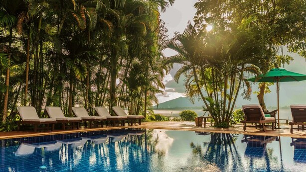 Un área de piscina con sillones reclinables y vista a un cuerpo de agua.
