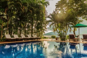 Un área de piscina con sillones reclinables y vista a un cuerpo de agua.
