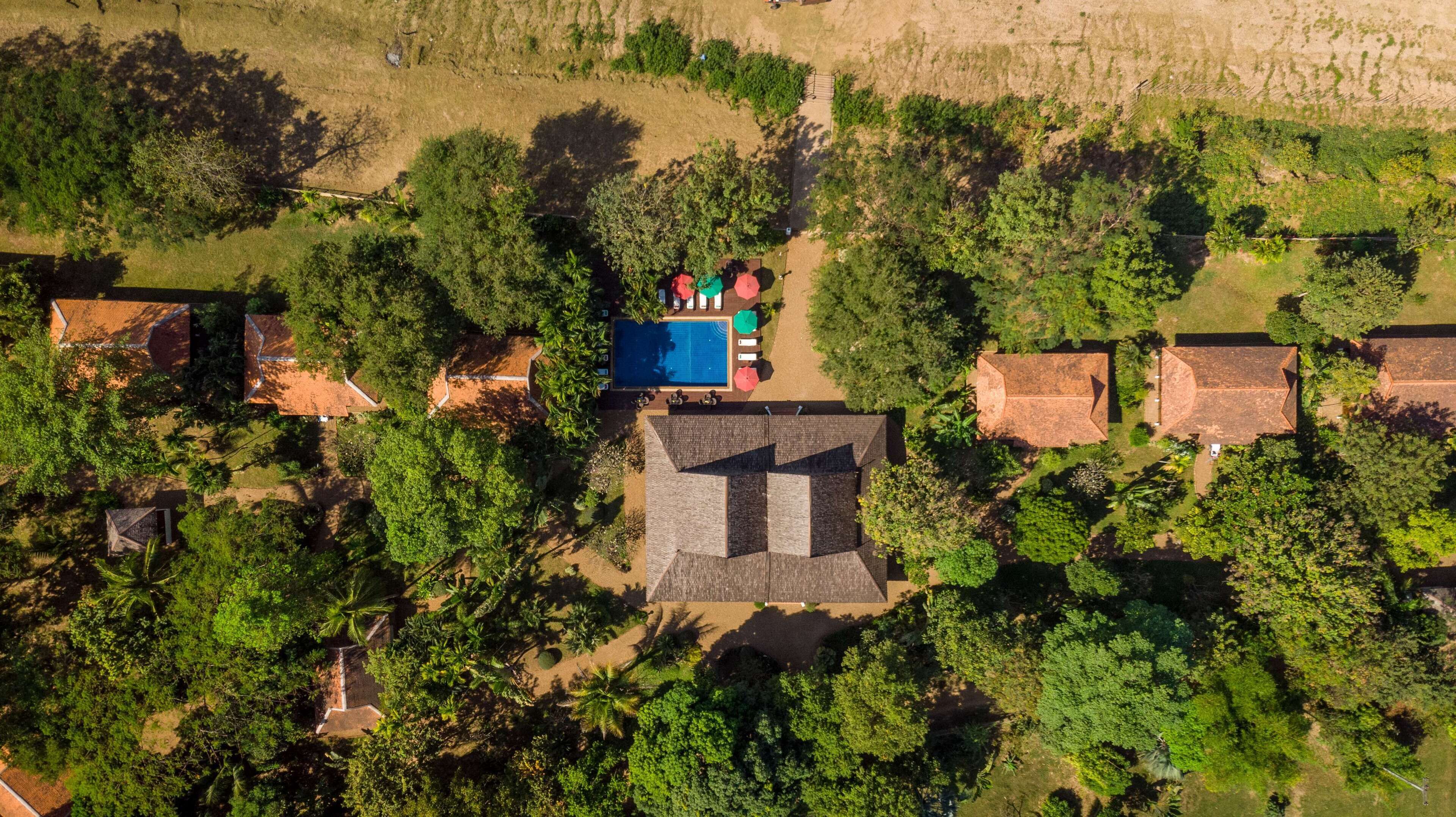 An aerial view of a resort with multiple bungalow-style buildings, a swimming pool, and lush greenery.