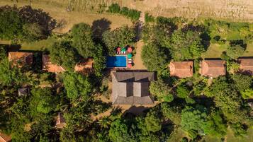 An aerial view of a resort with multiple bungalow-style buildings, a swimming pool, and lush greenery.