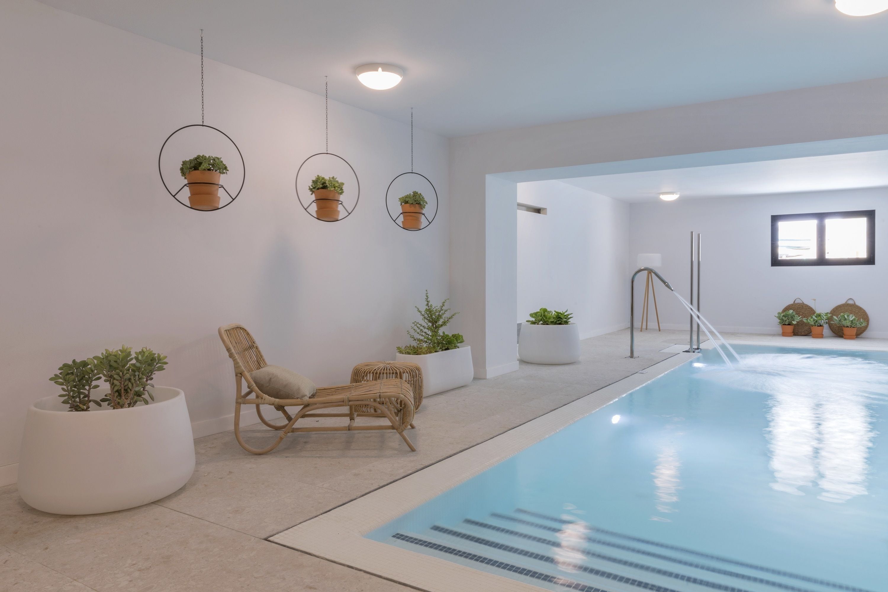 A modern indoor pool area with a lounge chair, potted plants, and a clear pool.