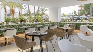 An outdoor dining area with tables and chairs, surrounded by greenery and palm trees. - Hotel HM Ayron Park – Adults Only (Palma de Mallorca)