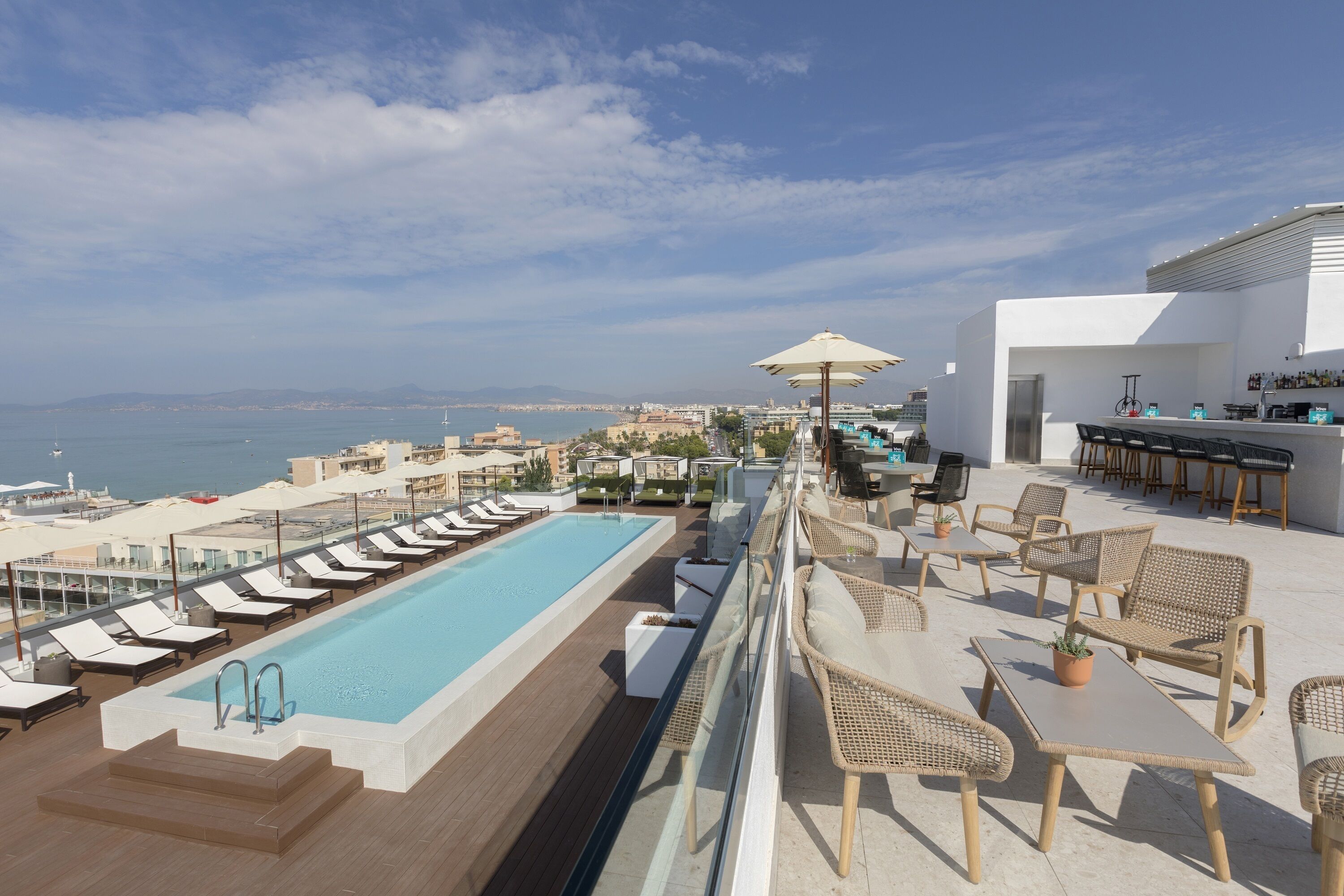 Un área de piscina en la azotea con sillones de descanso y un bar.