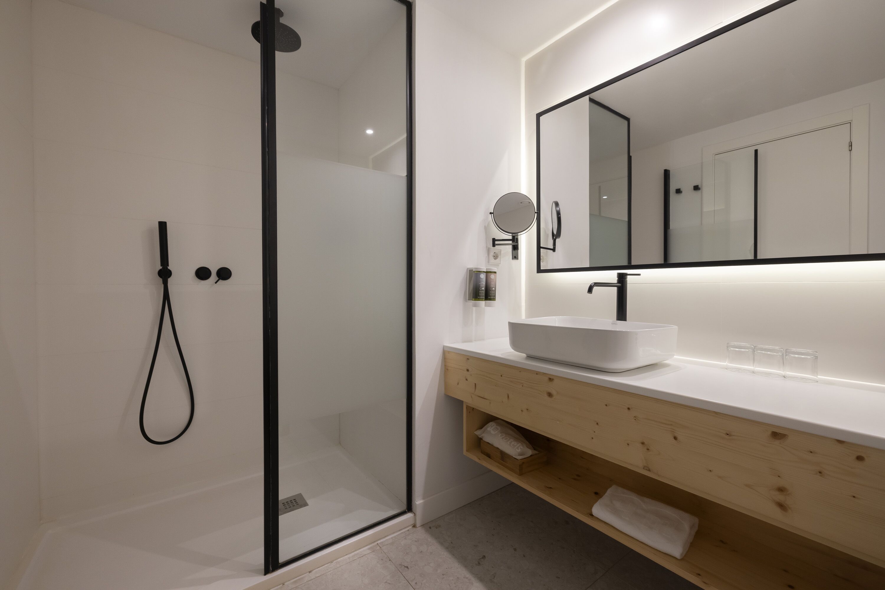 Ein modernes Badezimmer mit Duschkabine aus Glas, einem weißen Waschbecken und einem hölzernen Waschtisch.