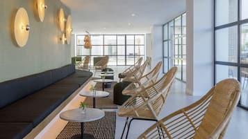 Un área de descanso moderna con sofá, sillas de mimbre, mesitas pequeñas e iluminación empotrada.