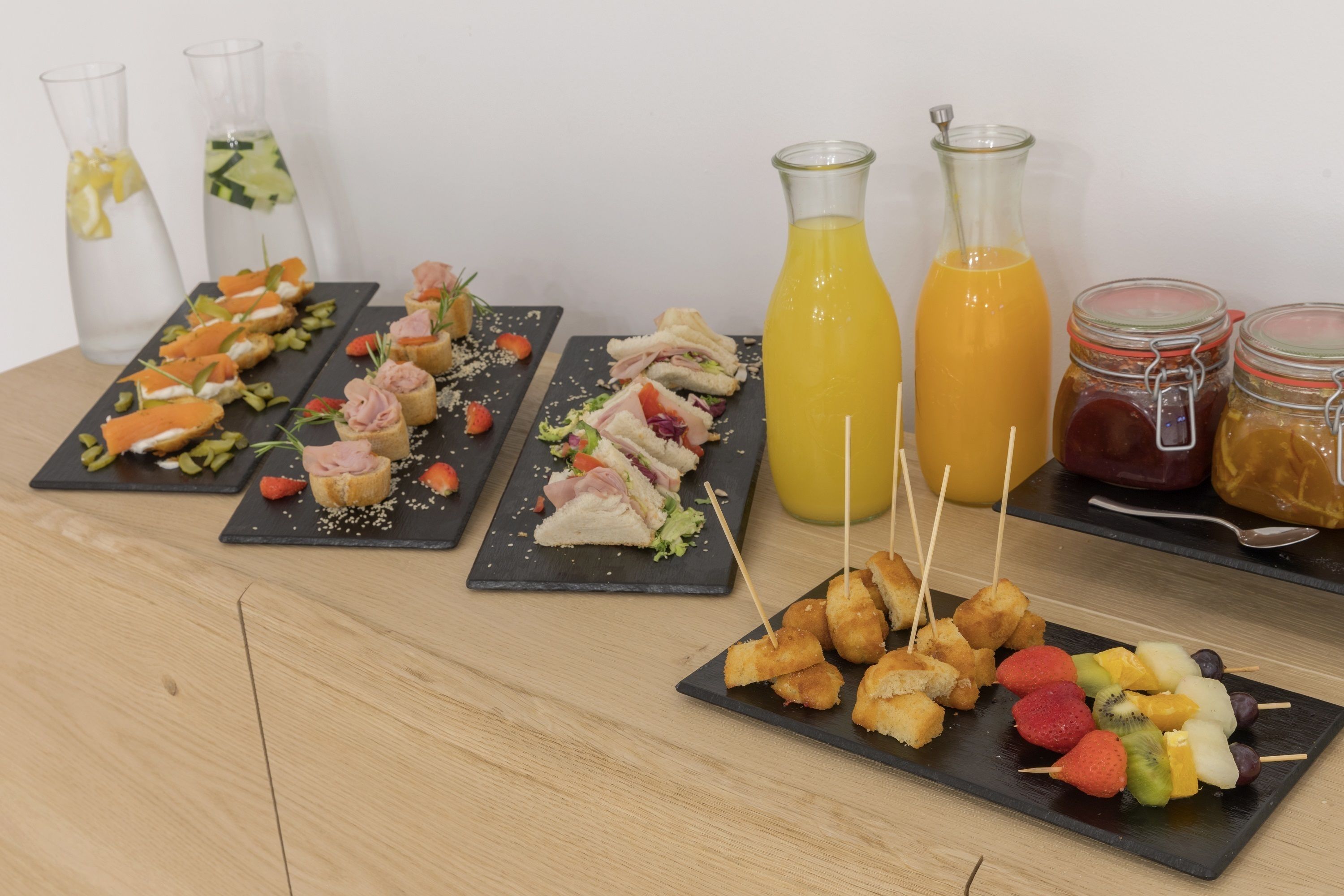Una mesa con diversos alimentos y bebidas, como sándwiches, brochetas de fruta y botellas de jugo.