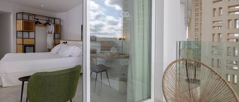 A modern hotel room with a bed, a green chair, a glass table, and a glass door leading to a balcony.