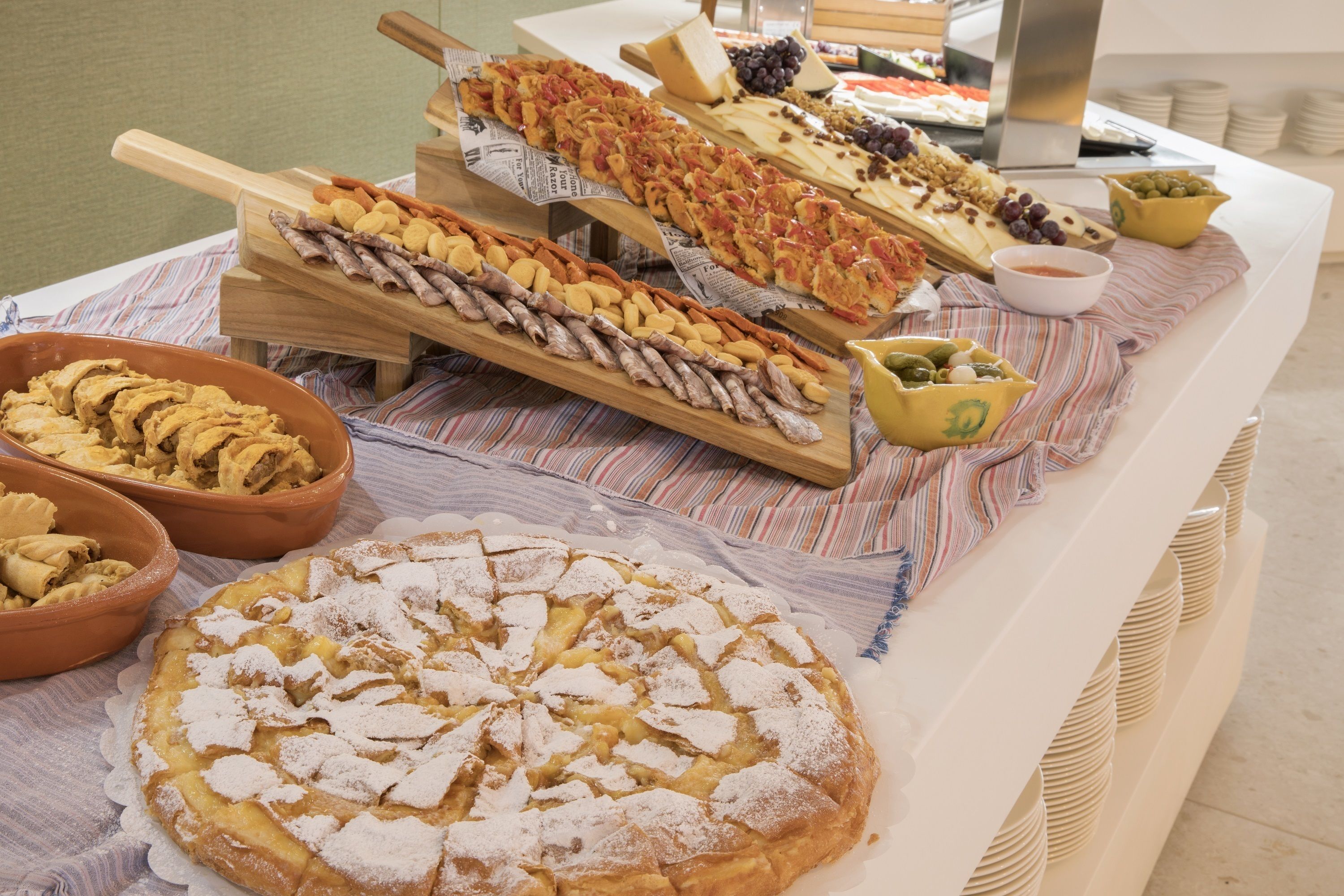 A buffet table with various dishes including a large apple pie, cheese boards, and assorted meats.