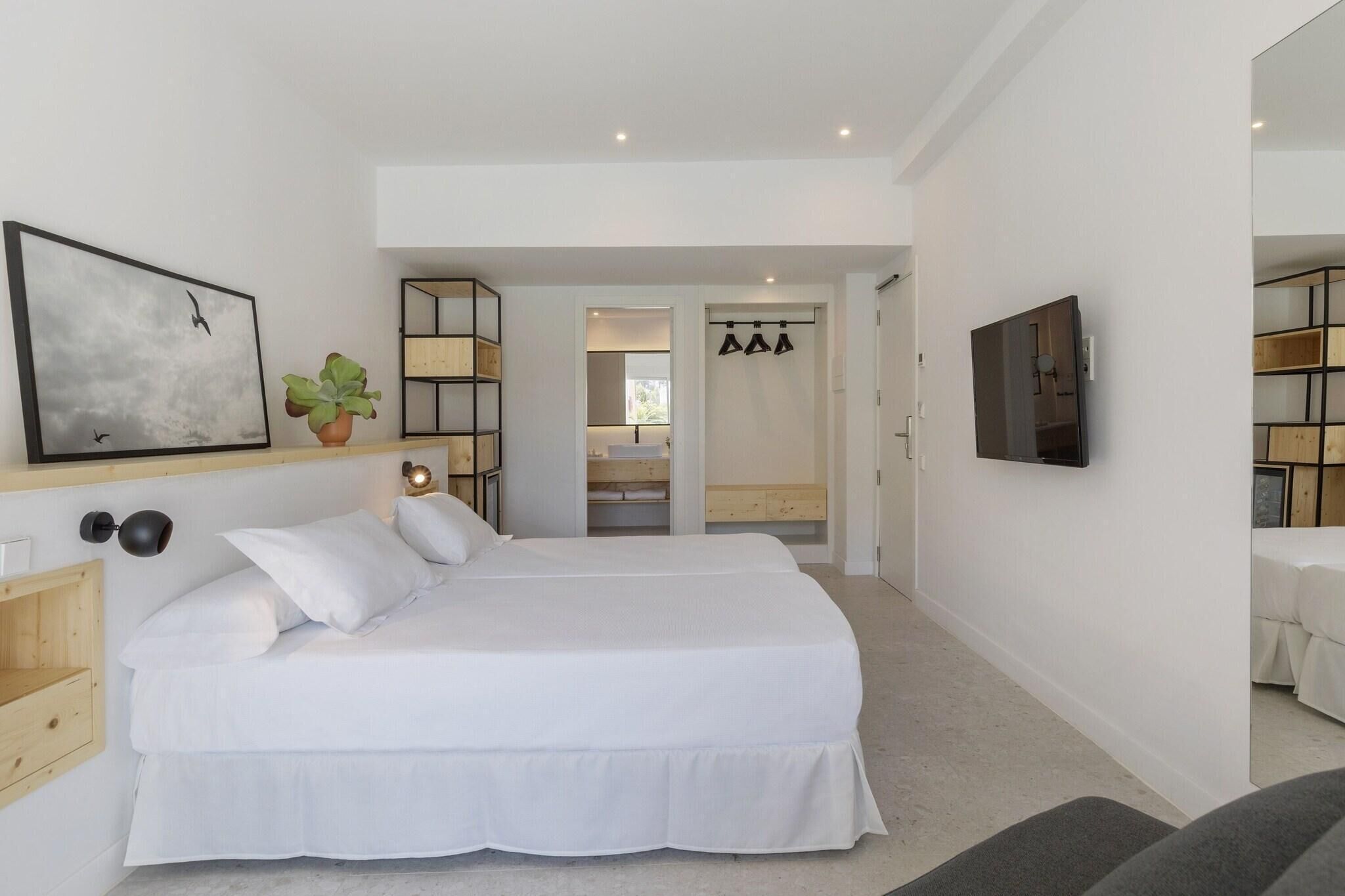 A modern bedroom with a large bed, a TV, a plant, and a walk-in closet.