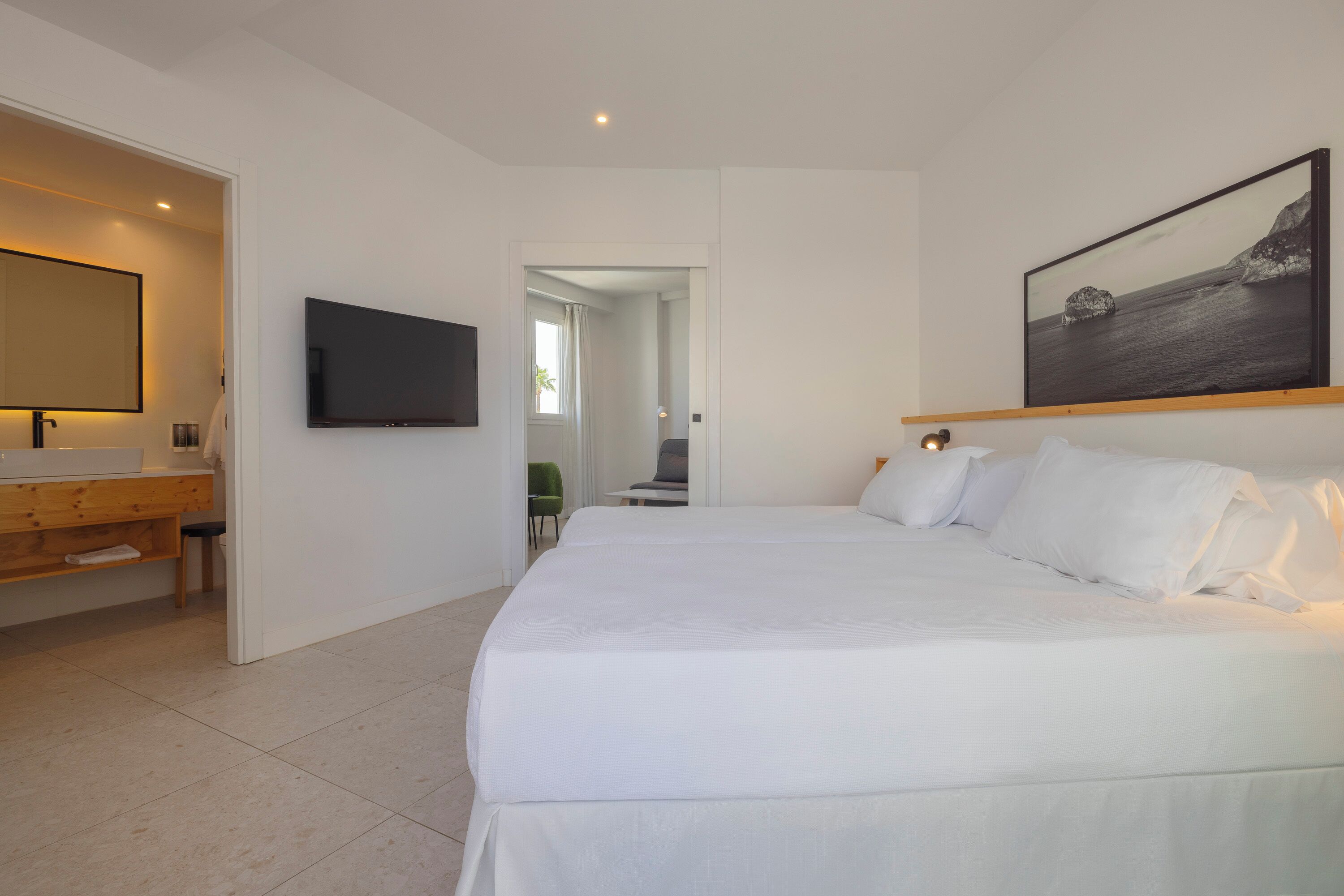 Una habitación de hotel moderna con una cama grande, un televisor de pantalla plana montado en la pared, un escritorio de madera y un baño con espejo.