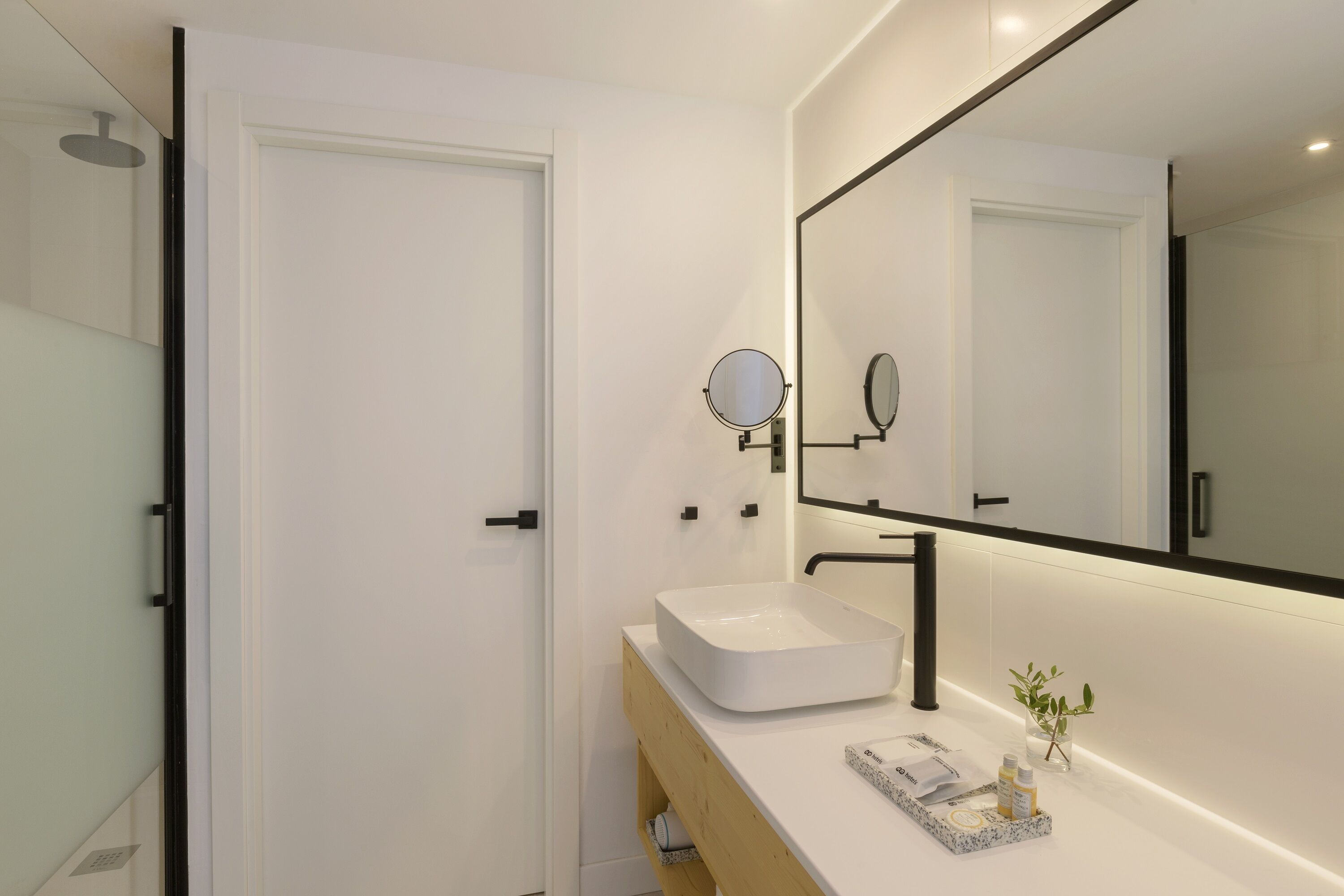 A modern bathroom with a white sink, a large mirror, and a wooden vanity.
