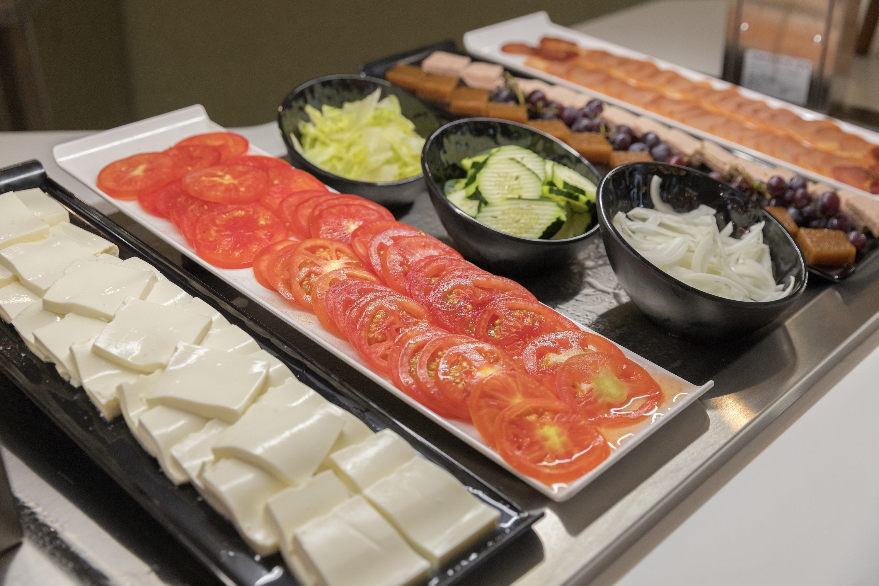 En buffet med forskellige retter, blandt andet skiveskåret tomat, agurk og ost.