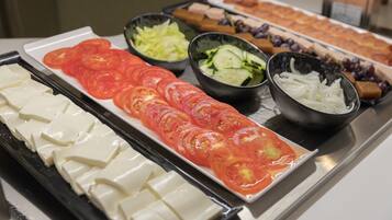 En buffet med forskellige retter, blandt andet skiveskåret tomat, agurk og ost.