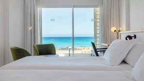 A hotel room with a bed, a table, two chairs, and a view of the ocean.