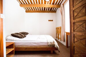 A single bed with a wooden frame, a white mattress, and a brown blanket. There is a wooden shelf to the left of the bed, and a wooden door with a geometric pattern to the right. - Langley Hotel La Vieille Ferme (La Salle-les-Alpes)