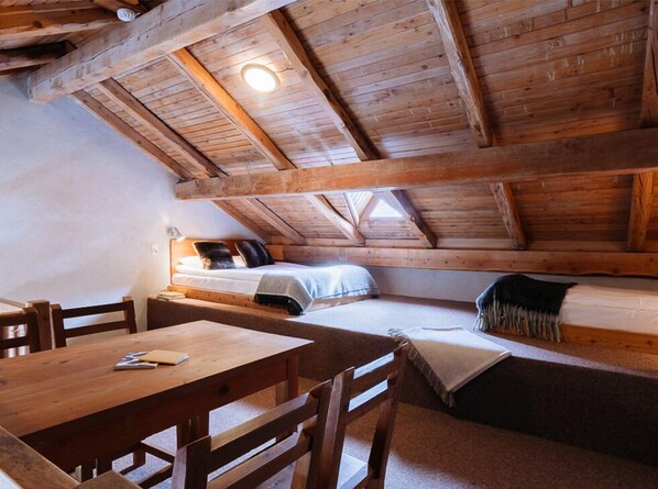 Un dormitorio acogedor en el ático, con techo de madera, una cama con almohadas, una mesita de noche y una silla.