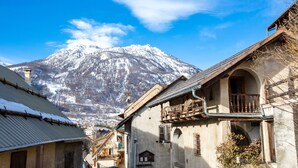 A narrow street with traditional buildings, a snow-covered mountain in the background, and a clear blue sky. - Langley Hotel La Vieille Ferme (La Salle-les-Alpes)
