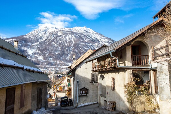 A narrow street with traditional buildings, a snow-covered mountain in the background, and a clear blue sky. - Langley Hotel La Vieille Ferme (La Salle-les-Alpes)