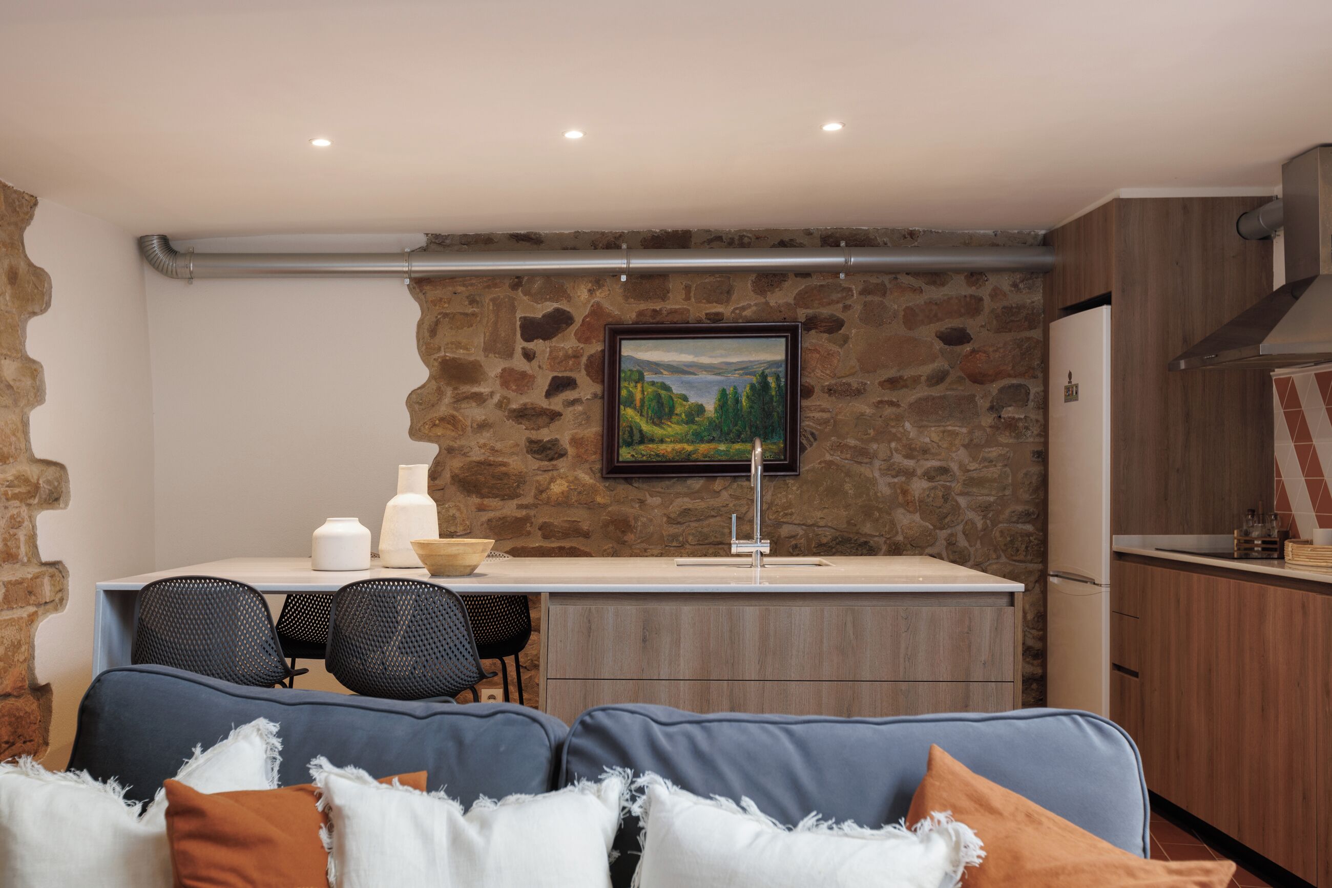 A modern kitchen with a stone wall, a dining area with a table and chairs, and a living area with a sofa.