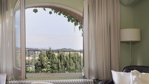 A room with a large arched window, a radiator, a leather sofa, a chair, and a table with books. - Encís d Empordà (Corca)