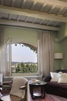 A room with a large arched window, a radiator, a leather sofa, a chair, and a table with books.