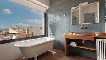 A bathroom with a freestanding bathtub, a wooden vanity, a mirror, and a view of the cityscape.