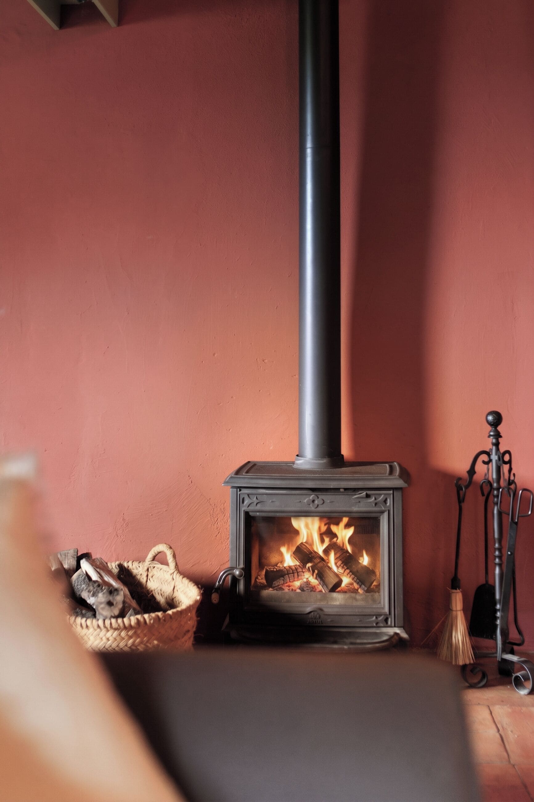 A wood-burning stove with a chimney, a basket of firewood, and a broom.