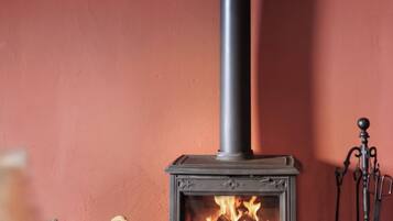 A wood-burning stove with a chimney, a basket of firewood, and a broom.