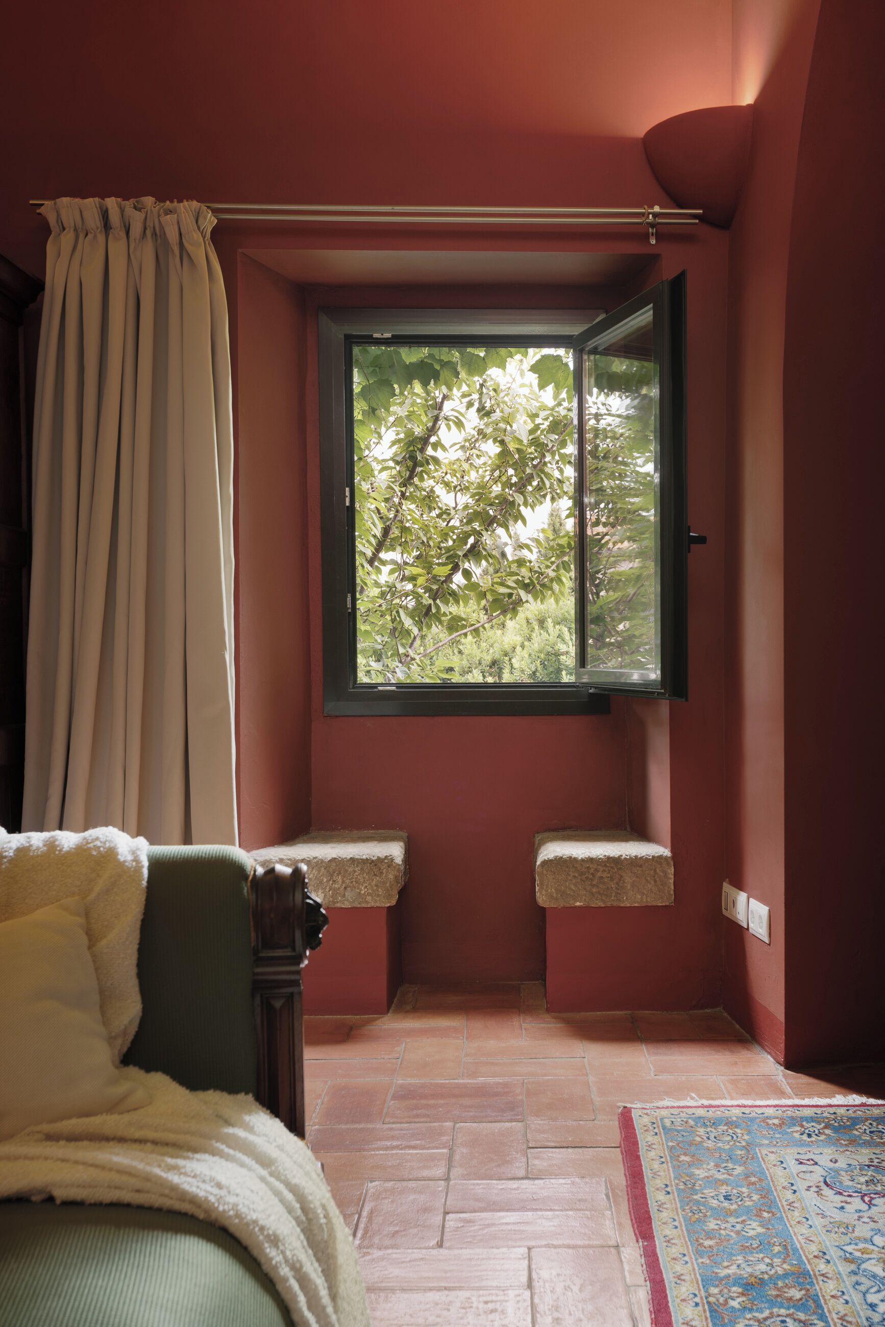 Una habitación con ventana, cama, banco y alfombra.