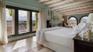 A bedroom with a large bed, a TV, a desk, and a view of the city through large windows. - Encís d Empordà (Corca)