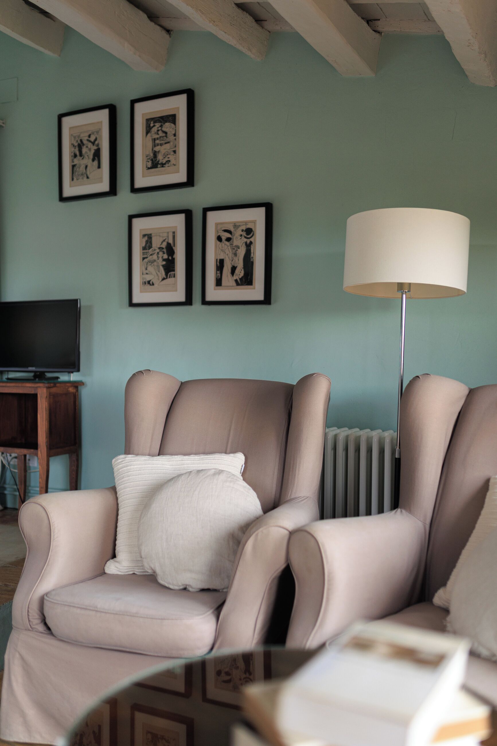 Un soggiorno con una poltrona beige, una lampada da terra e opere d'arte incorniciate appese al muro.