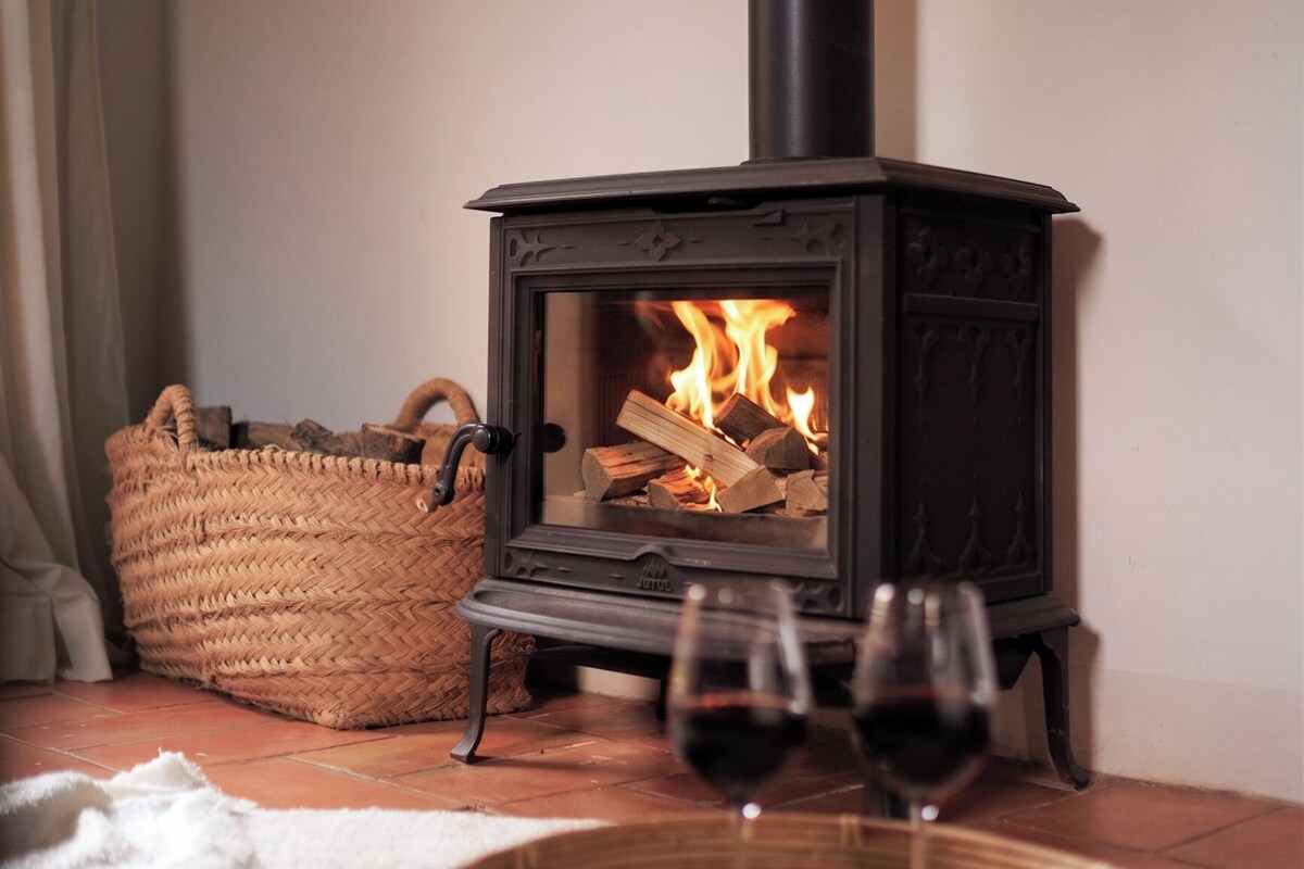A wood-burning stove with flames, a woven basket, and two glasses of red wine on a tray.