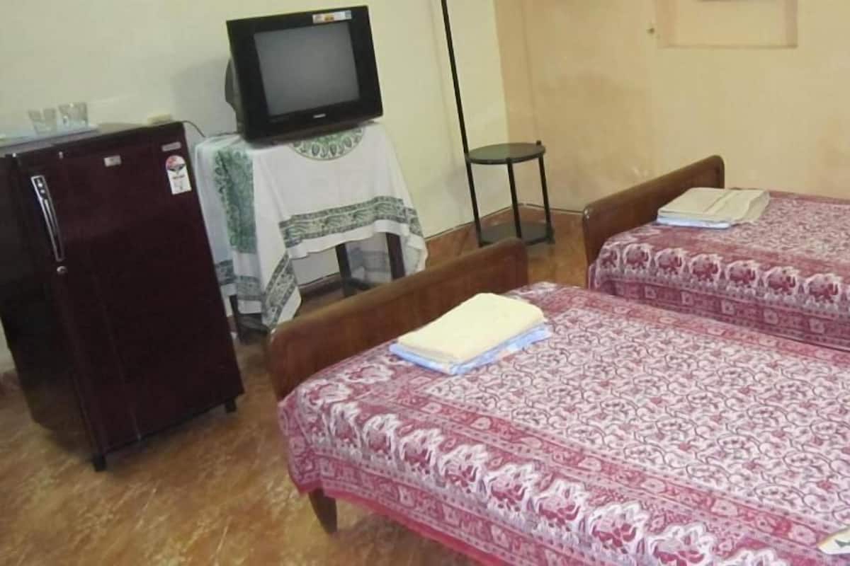 Een kamer met twee bedden, een televisie op een tafeltje en een koelkast.