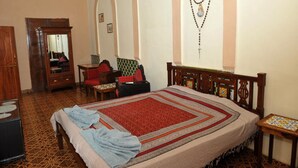 A bedroom with a large bed, a wooden wardrobe, a small table, and a chair. - Hotel Vivenda Rebelo (Panaji)